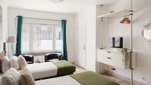 Una habitación de hotel con dos camas, un escritorio con televisor, un armario y una ventana con cortinas.