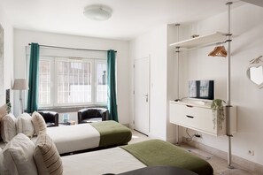 Ein Hotelzimmer mit zwei Betten, einem Schreibtisch mit Fernseher, einem Kleiderschrank und einem Fenster mit Vorhängen.