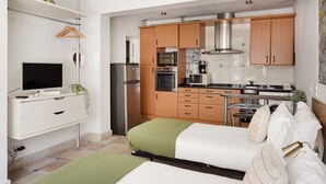 Un apartamento estudio compacto con kitchenette, una cama con manta verde, un televisor y un pequeño comedor.