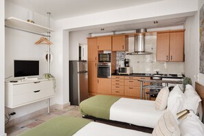 Ein kompaktes Studioapartment mit Küchenzeile, einem Bett mit grüner Tagesdecke, einem Fernseher und einer kleinen Essecke.