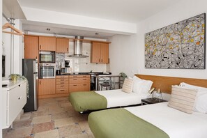 Ein kompaktes Hotelzimmer mit Küchenzeile, zwei Einzelbetten, einem großen abstrakten Gemälde und Blick auf die Stadt.