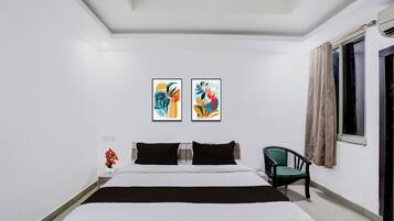 Ein Hotelzimmer mit einem Bett, zwei Bildern an der Wand, einem Sessel und einem fenster mit Vorhängen.