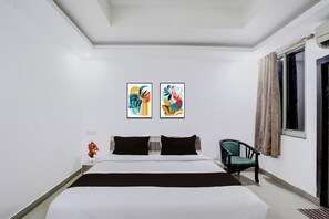 A hotel room with a bed, two paintings on the wall, a chair, and a window with curtains.