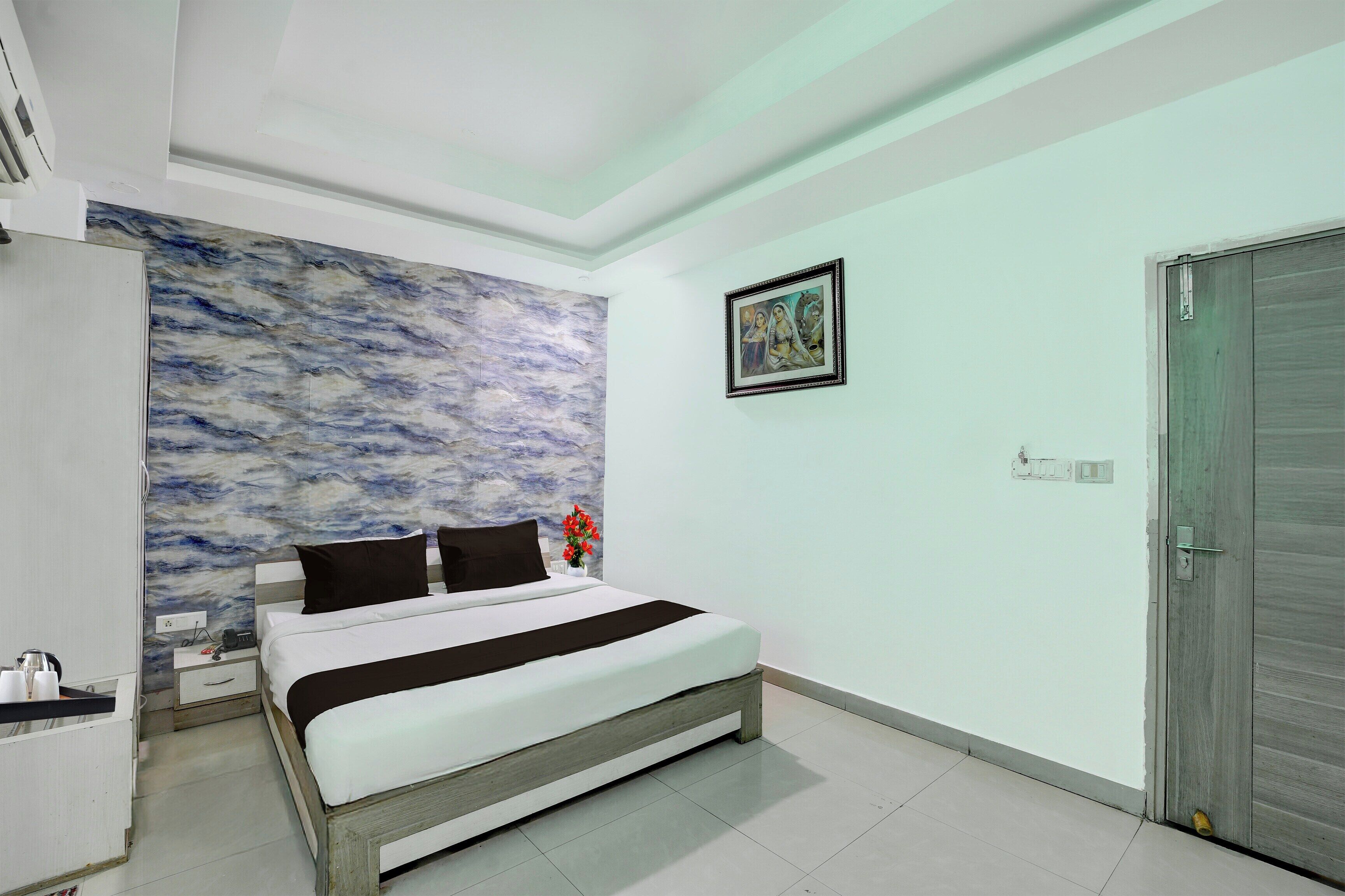 A bedroom with a bed, a wall with a marble-like texture, a door, and a framed picture on the wall.