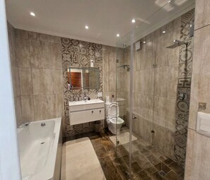 Ein modernes Badezimmer mit einer gläsernen Duschkabine, einer Badewanne und einem Waschtisch mit Spiegel.