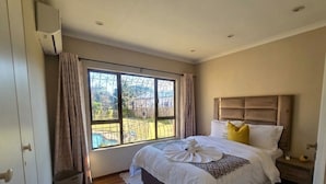Un dormitorio con un ventanal grande, una cama con ropa de cama blanca, suelo de madera y cabecero.