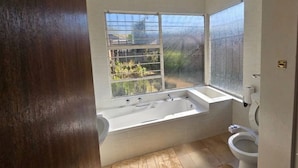 Un baño moderno con una bañera grande, un inodoro y un ventanal con vistas a la vegetación.