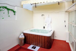 Un espacio pequeño y privado con un jacuzzi de madera, un perchero y un cubo de basura.