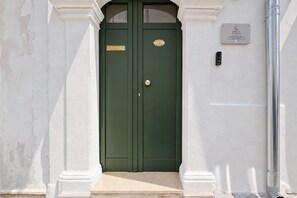 Een groene dubbele deur met een koperen handvat en een plaquette, in een wit gebouw met een klein opstapje.