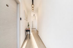 A hallway with a wooden floor, a small table with a vase of flowers, and a wall-mounted light fixture. - Domus dell’Angelo 2: comfort and authenticity in the heart of Monte Sant’Angelo (Monte Sant'Angelo)