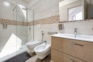 Ein modernes Badezimmer mit Duschkabine aus Glas, einem Bidet, einer Toilette und einem Waschtisch mit Spiegel.