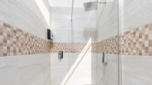 Un baño moderno con cabina de ducha de vidrio, ducha de mano y secador de manos integrado en la pared.
