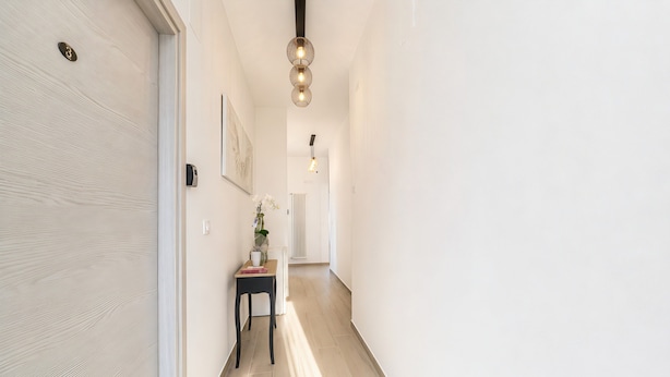 Un pasillo con piso de madera, una mesita con un florero y una lámpara de pared.