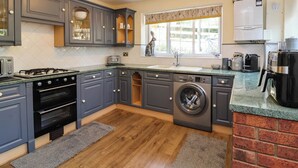A modern kitchen with grey cabinets, a built-in oven, a washing machine, and a coffee maker. - Pete's Place (Taunton)