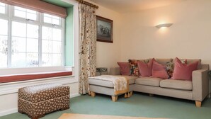 A living room with a sofa, ottoman, and a window with curtains. - Pete's Place (Taunton)
