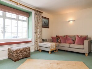 Ein Wohnzimmer mit einer Couch, einem Hocker und einem Fenster mit Vorhängen.