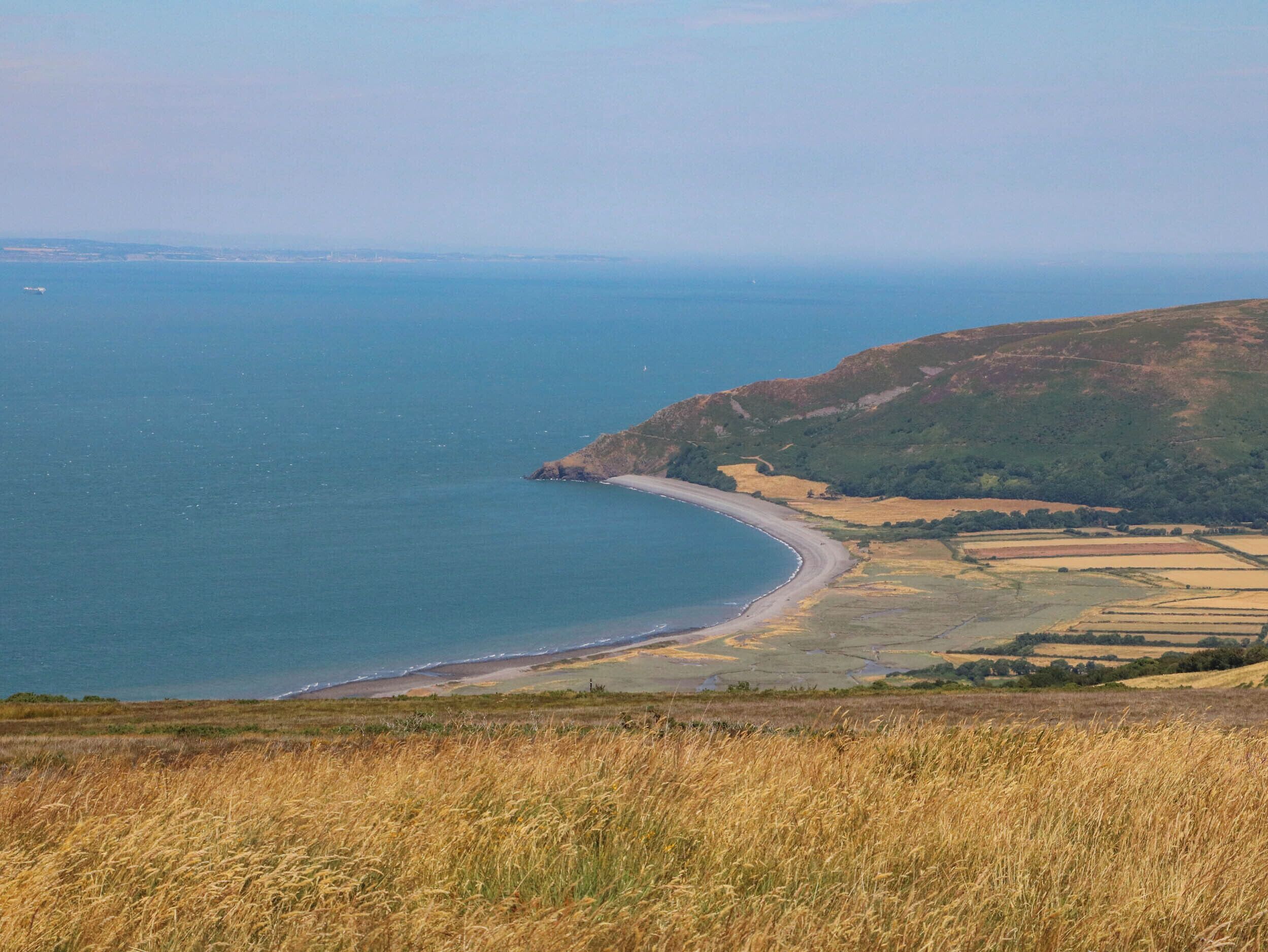 A coastal landscape with a beach, fields, and hills.