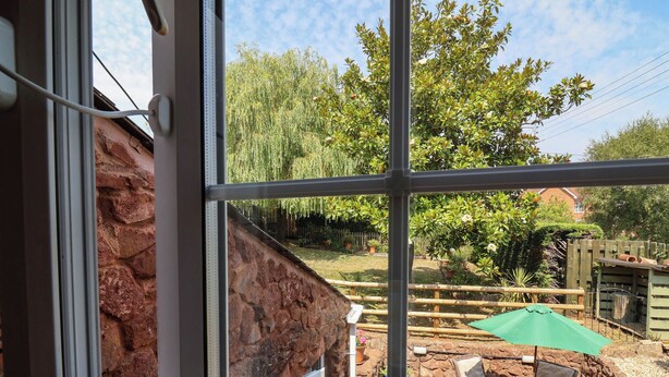 A view through a window of a stone wall, outdoor furniture, and a wooden fence in a garden. - Pete's Place (Taunton)