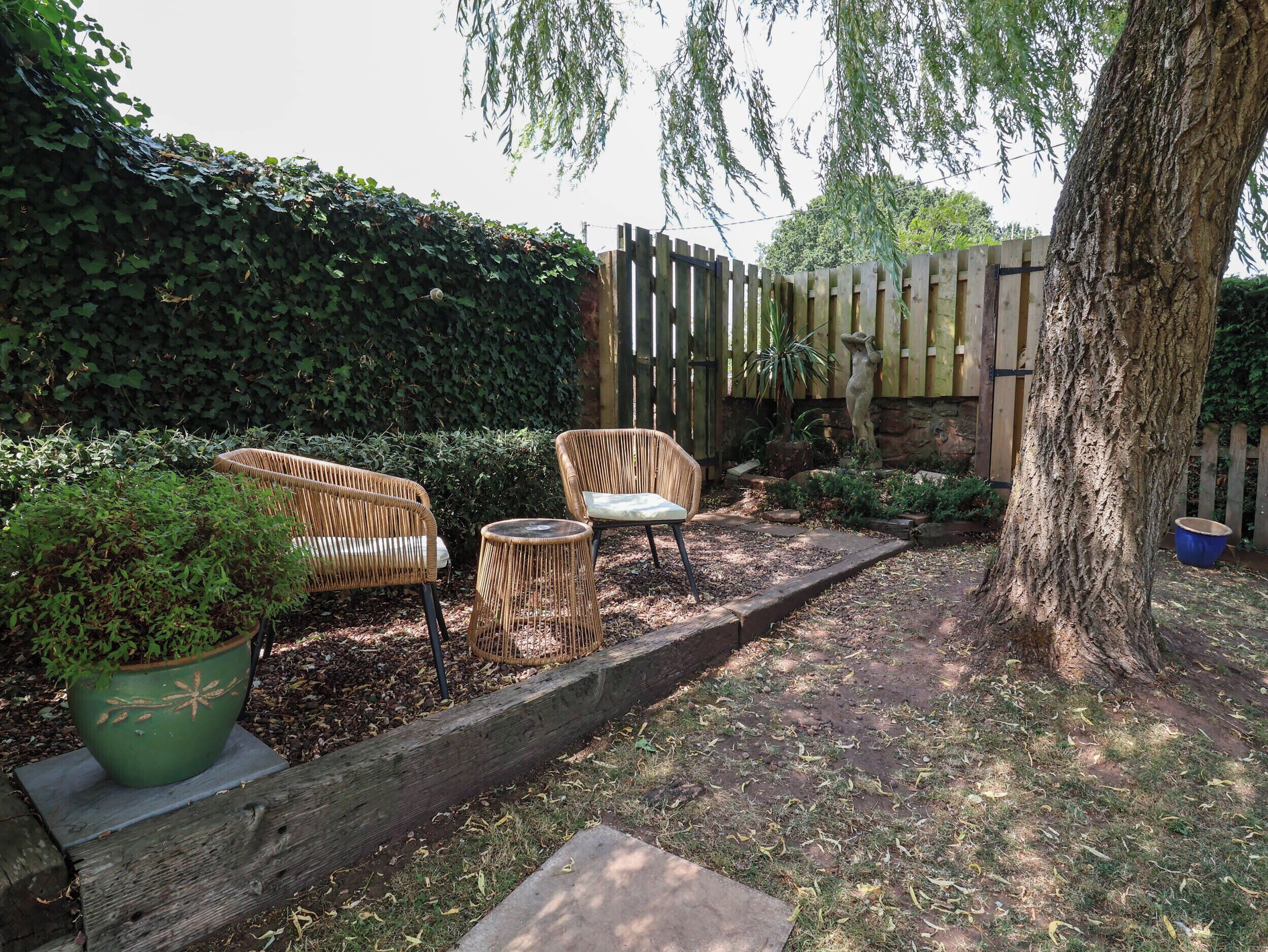 Ein Gartenbereich mit Korbmöbeln, einem Holzzaun und einem großen Baum.