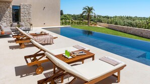 Ein Poolbereich mit Liegestühlen, einem Tisch mit Getränken und Blick auf eine üppige Landschaft.