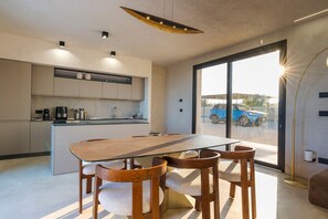 Eine moderne Küche mit integrierten Geräten, ein Essbereich mit Glastisch und Holzstühlen sowie eine große Schiebeglasdoor zum Außenbereich.