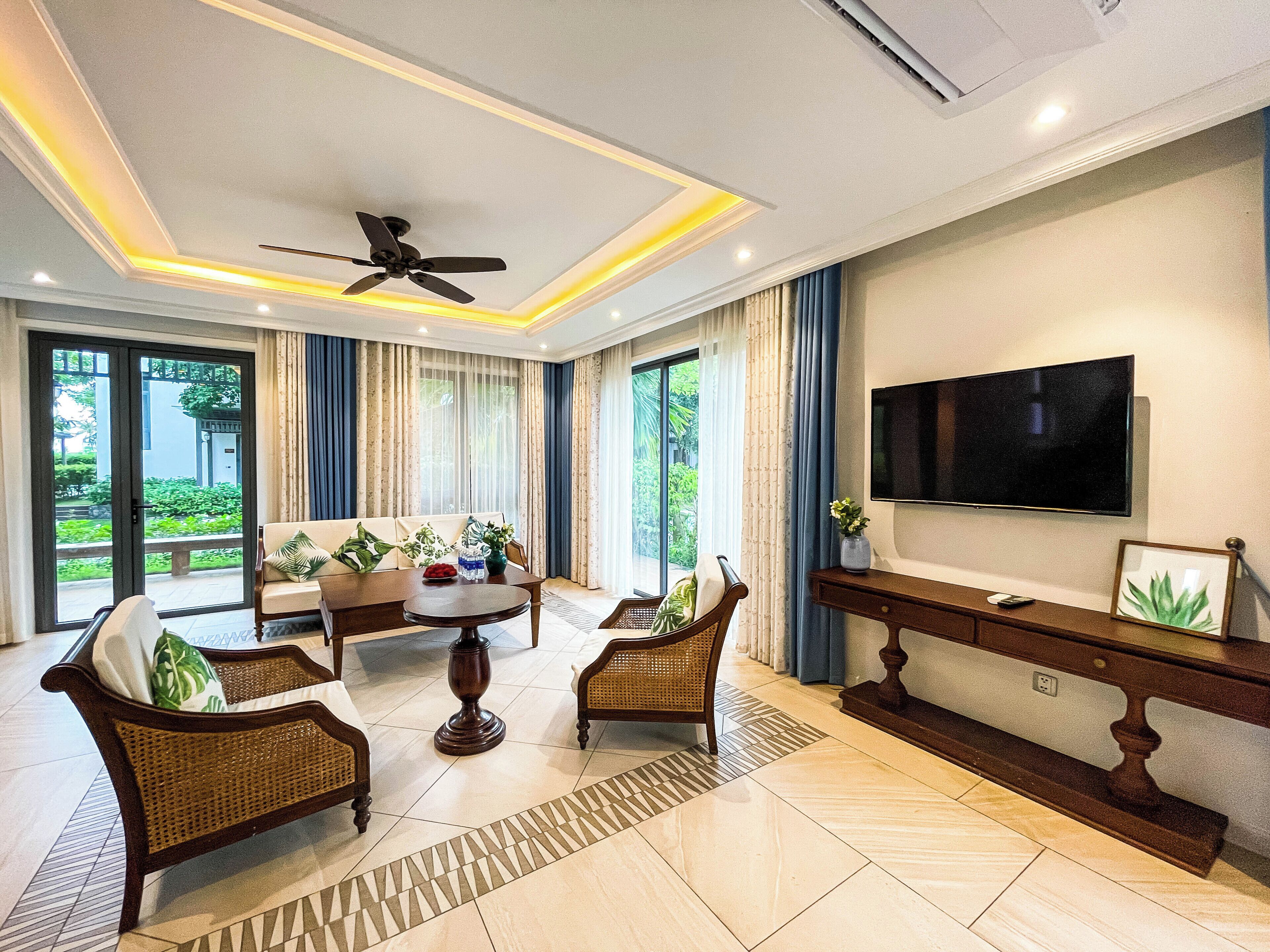 A modern living room with a ceiling fan, a flat-screen TV, and a sofa set.