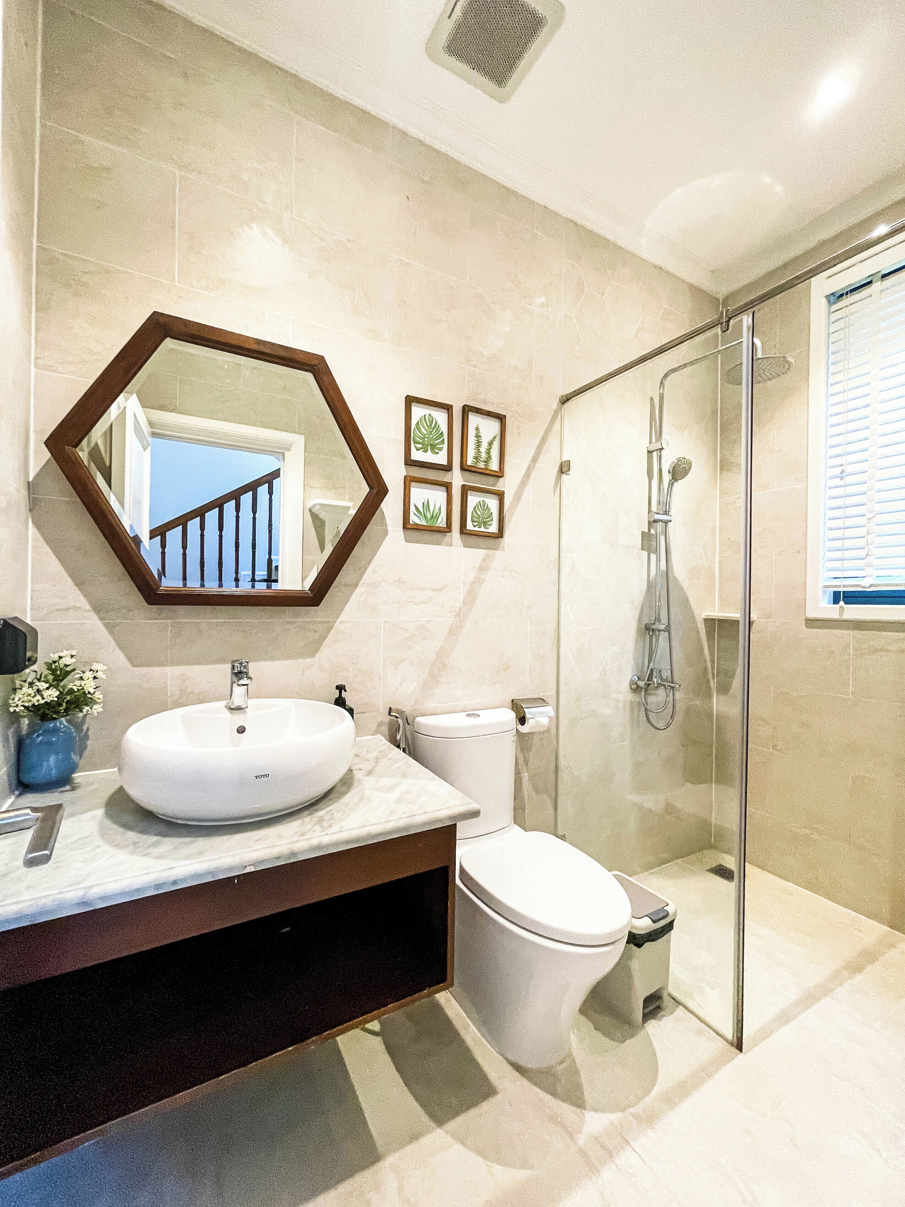 A modern bathroom with a large mirror, a round sink, a toilet, and a glass-enclosed shower.