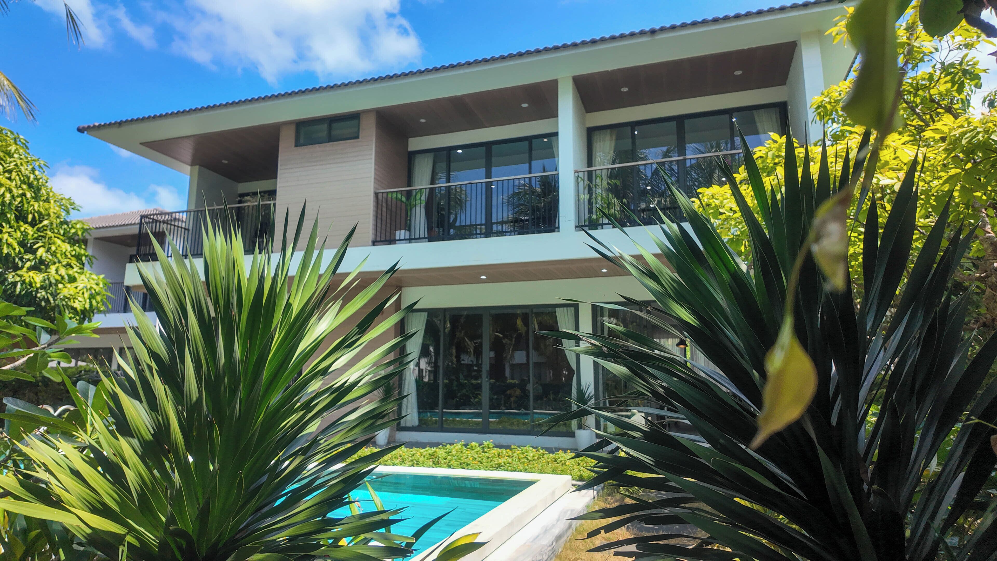 Un edificio residencial de dos pisos con piscina, rodeado de plantas tropicales.