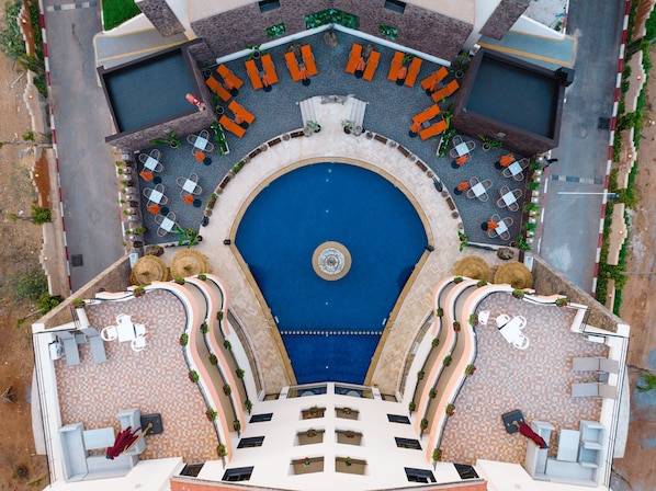 Vista cenital de un área de piscina hotelera con una piscina circular central, sillones lounge alrededor y una distribución simétrica de mesas y sillas.