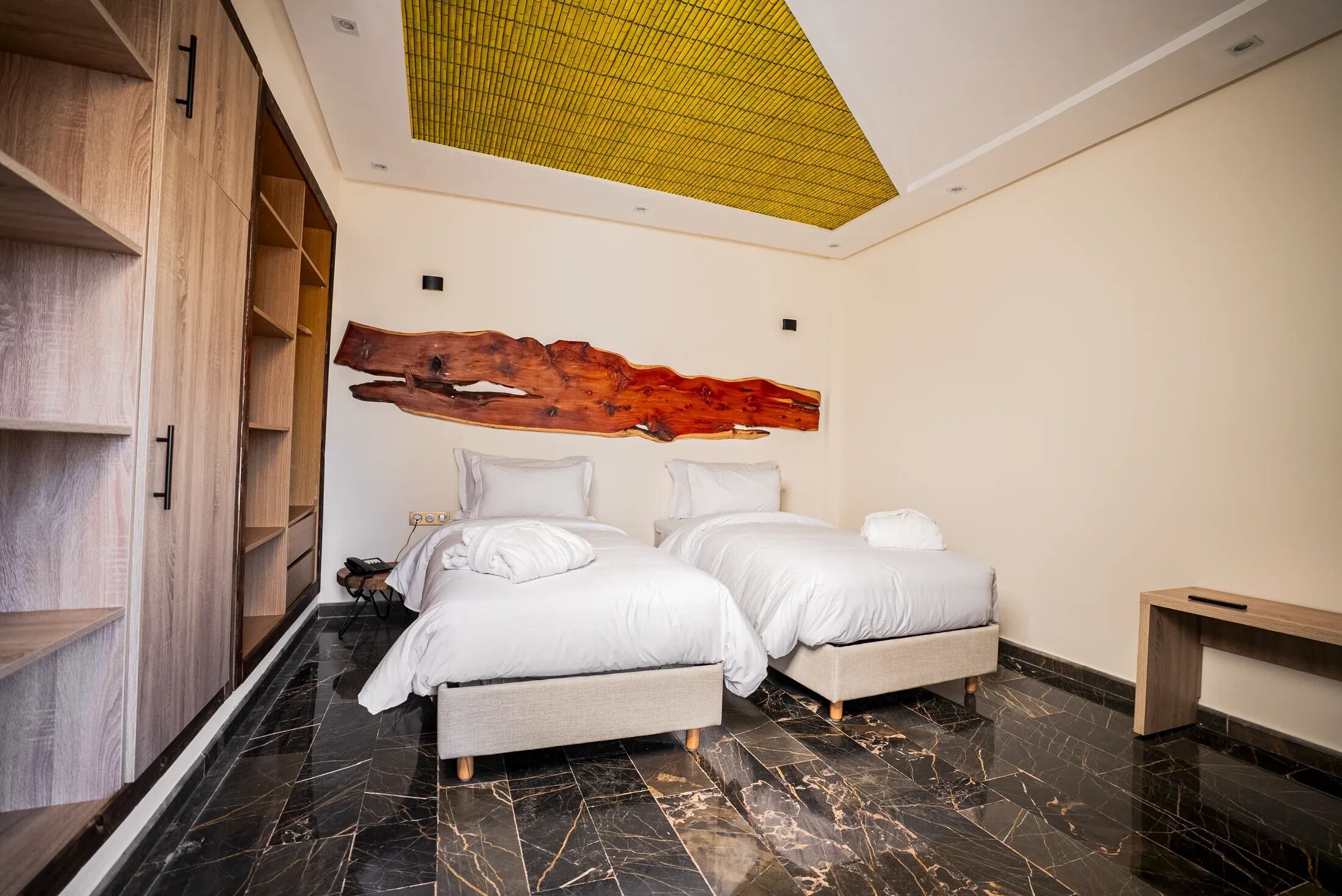 A modern bedroom with two beds, a wooden wardrobe, and a unique ceiling design.