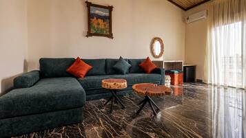 Una sala moderna con un sofá seccional, dos mesas redondas de madera, un cuadro, un espejo y un mueble bajo.
