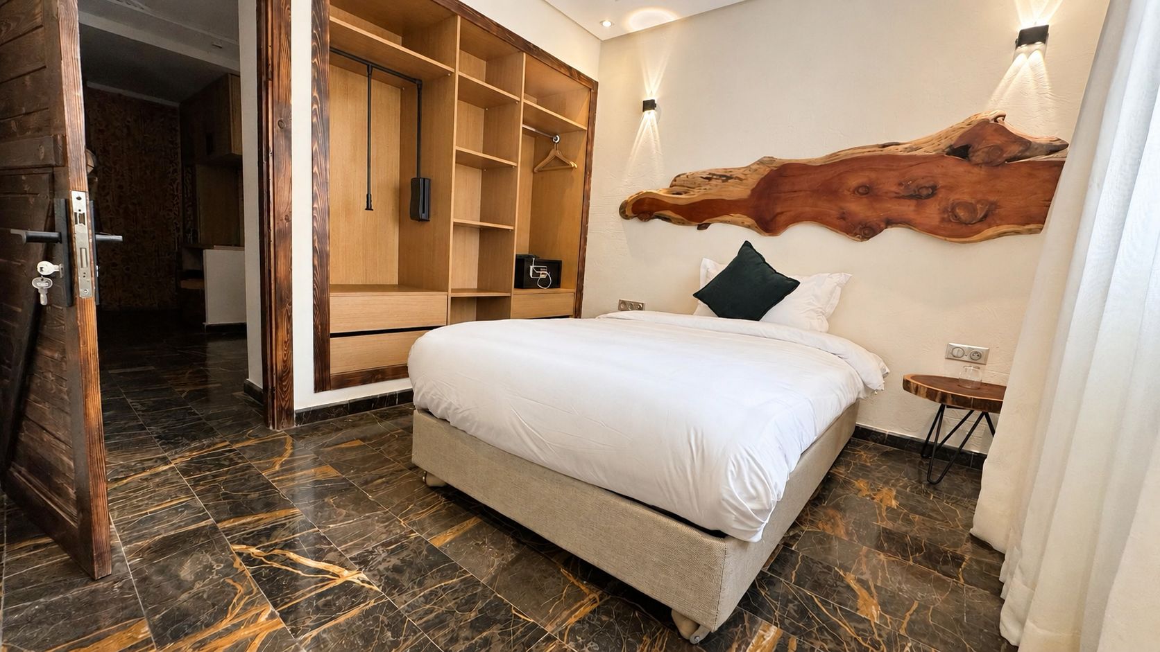 Un dormitorio con cama, armario de madera, lámpara de pared y una original cabecera de madera.