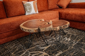Un sofá modular con un cojín con diseño de rostro, una mesa de centro redonda de madera con acabado natural, y un suelo con estampado de mármol.