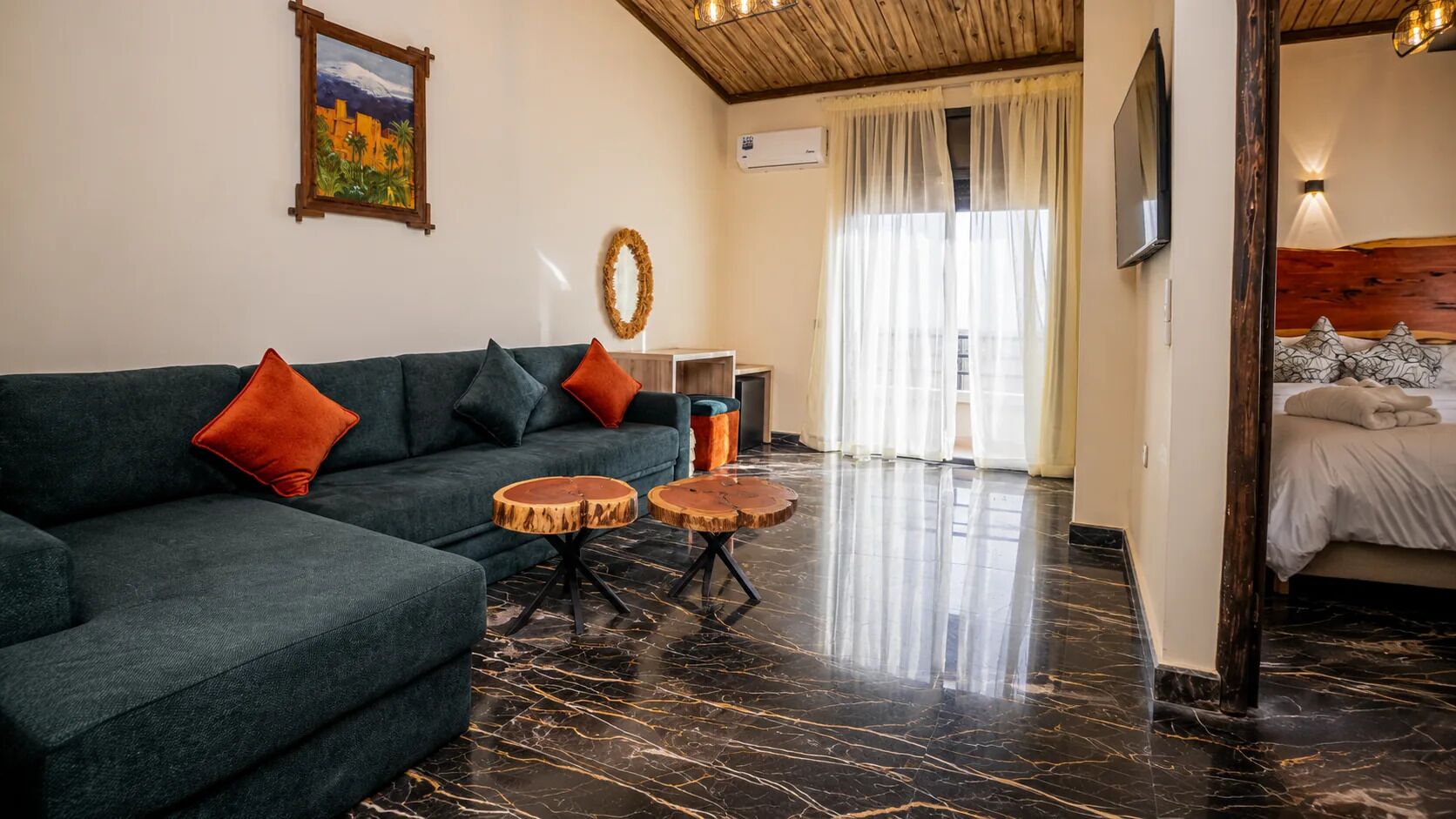 Una sala de estar moderna con un sofá, dos mesas redondas de madera, un cuadro y una cama al fondo.