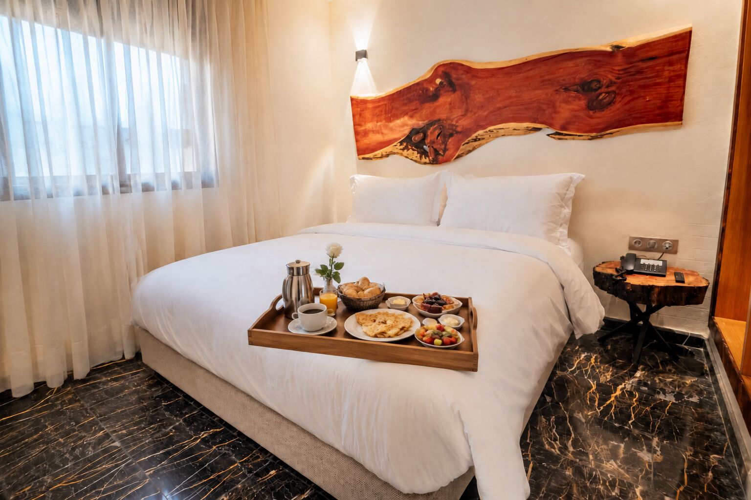 A hotel room with a bed, a tray with breakfast items, a coffee pot, and a bedside table with a phone and charger.
