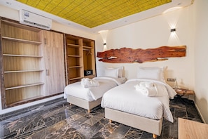 Habitación de hotel con dos camas, un armario, cabecero de madera, suelo de mármol y techo con un diseño de cuadrícula amarilla.