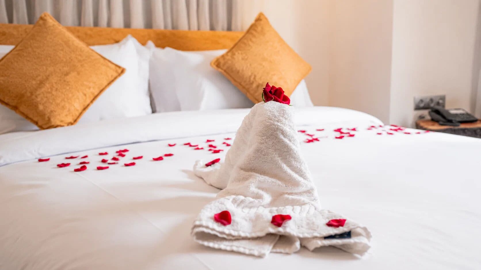 Een net opgemaakt bed met een witte handdoek en rozenblaadjes.