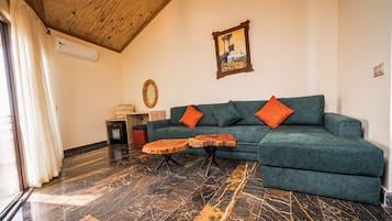 A living room with a green sofa, two orange cushions, a wooden coffee table, and a painting on the wall.