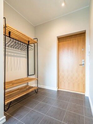 A hallway with a wooden bench, a coat rack with hanging clothes, a door, and tiled flooring. - Contemporary penthouse with balcony (Tallinn)