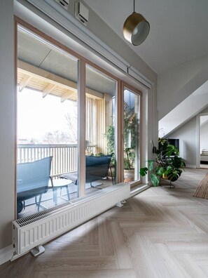 Ein Zimmer mit einer großen Schiebeglasdoor, die auf einen Balkon im Freien führt, einem Heizkörper, einer Pendelleuchte und einem Blumentopf.