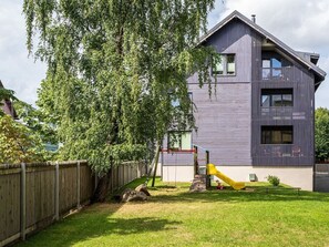A modern building with a flat roof, a wooden fence, and a playground with a slide. - Contemporary penthouse with balcony (Tallinn)