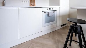 Una cocina moderna con armarios blancos, horno integrado y una pequeña mesa redonda con taburetes.