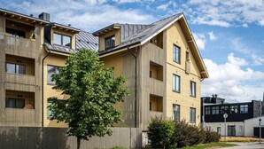 Un moderno edificio residencial de varios pisos con balcones, una cerca de madera y un árbol en primer plano.