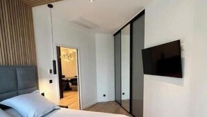 A modern bedroom with a large bed, a television mounted on the wall, and a wooden ceiling design. - Spacious, recently renovated loft with air conditioning (Île-de-France)