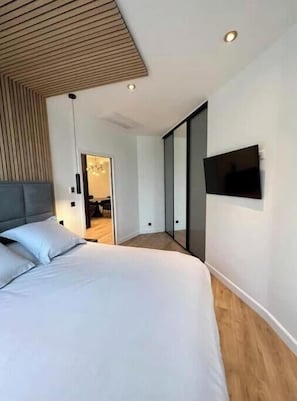 Ein modernes Schlafzimmer mit einem großen Bett, einem an der Wand montierten Fernseher und einer Holzbalkendecke.