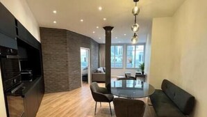 A modern kitchen with a built-in oven, a dining area with a round table and chairs, and a view of the outside through large windows. - Spacious, recently renovated loft with air conditioning (Île-de-France)