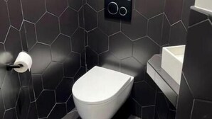 A modern bathroom with a white toilet, black hexagonal tiles, and a black wall-mounted flush control. - Spacious, recently renovated loft with air conditioning (Île-de-France)