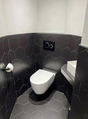 Ein modernes Badezimmer mit Toilette, schwarzen sechseckigen Fliesen und einem an der Wand befestigten Spülknopf.