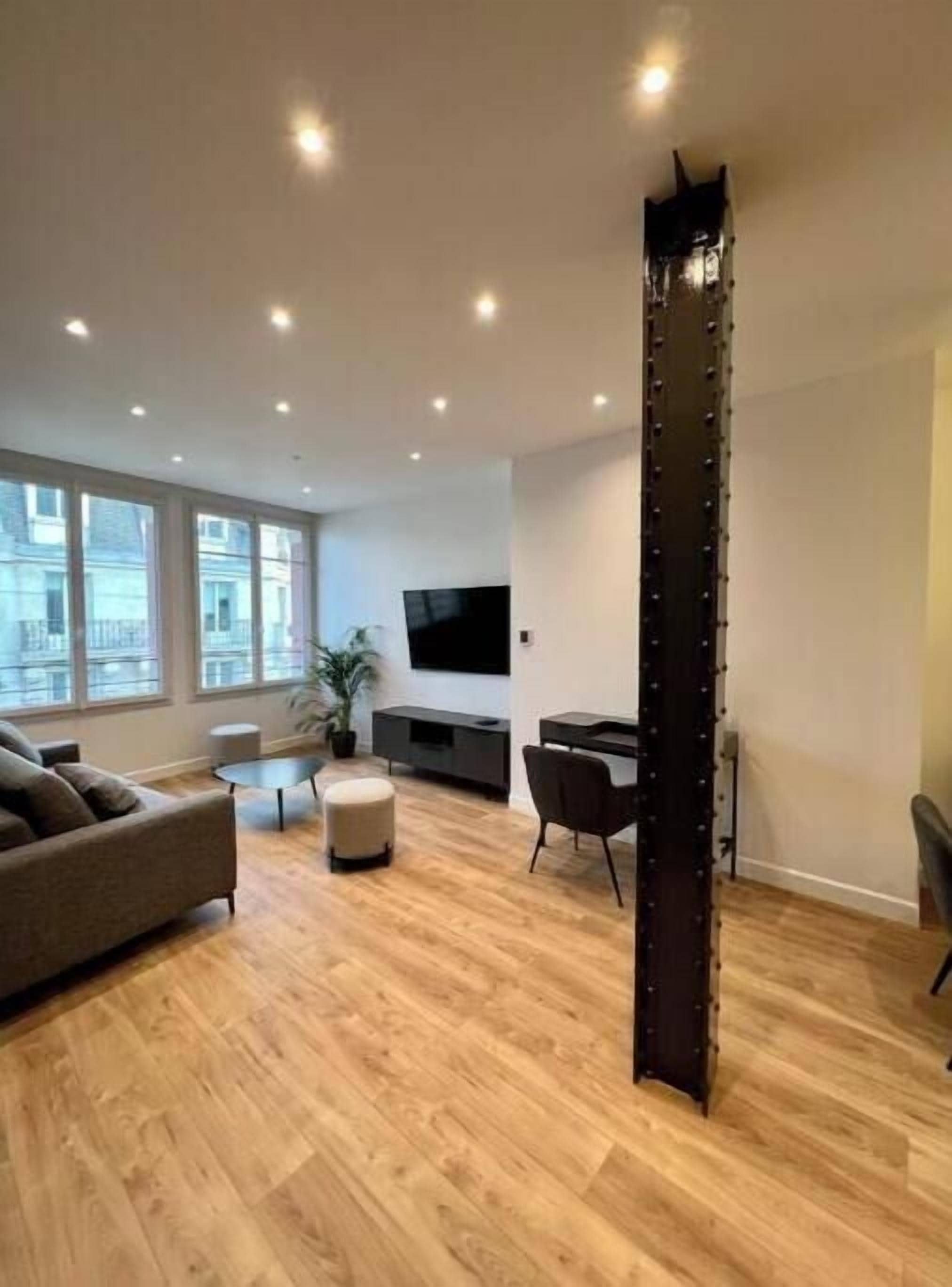 A modern living room with a wooden floor, a sofa, a coffee table, and a TV mounted on the wall.