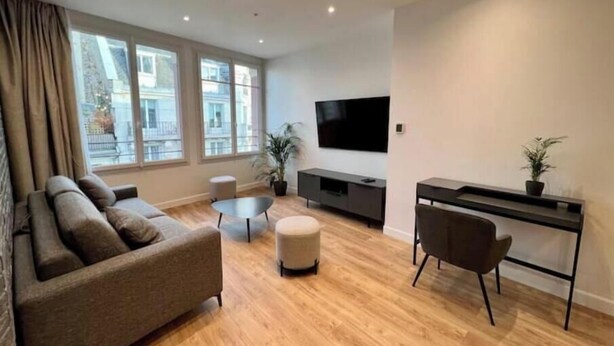 A modern living room with a sofa, ottoman, and a desk with a chair. - Spacious, recently renovated loft with air conditioning (Île-de-France)